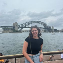 girl wearing a black top and a jean skirt standing in front of Sydney Harbor Bridge