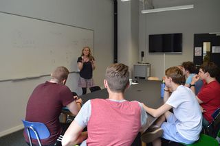 Students in class while a teacher lectures at a whiteboard