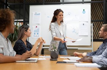 Female finance intern presenting to coworkers at a whiteboard in a conference room