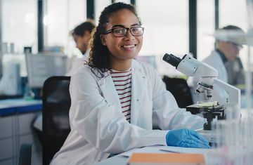 A student intern sitting at a microscope in a lab