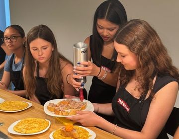 Girls using whipped cream siphon for red pepper foam.