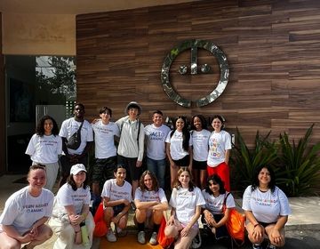 A group of students and group leaders in white t-shirts stand in front of the AMANC building in Merida, Yucatan. 