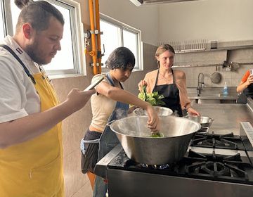 two students stand over a stove as they participate in a cooking class