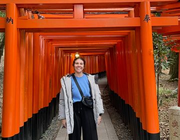 girl standing below the orange Torii Gates in Japan