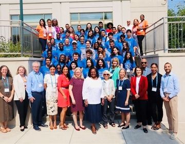 Group photo of participants, organizers, and special guests at the 2024 Young Civic Leadership Summit. The diverse group, wearing blue CIEE t-shirts, stands together on the steps outside a building, smiling and celebrating the successful event.