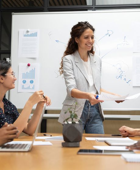 Female finance intern presenting to coworkers at a whiteboard in a conference room