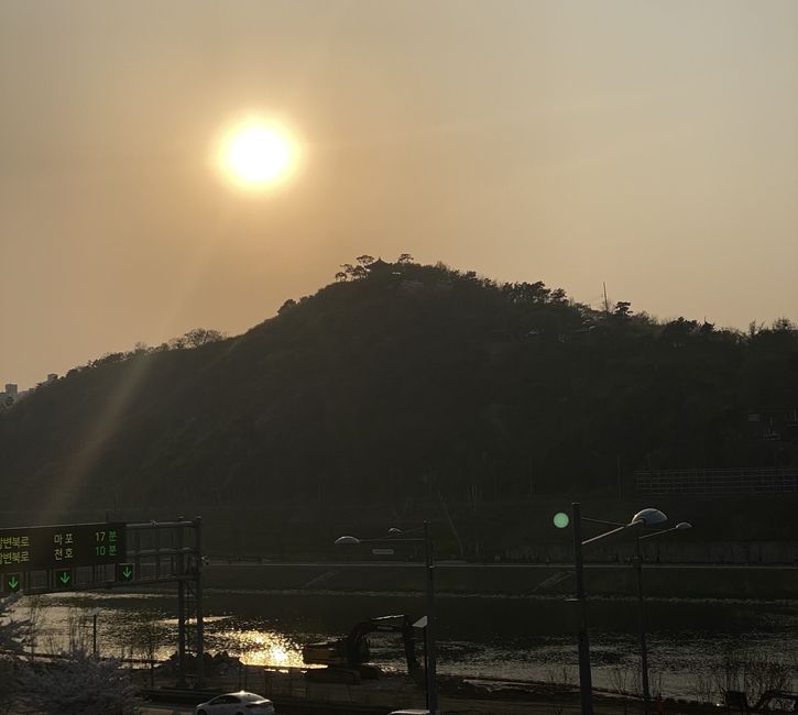 unarmed mountain, with the sun on the top left, a river at the bottom of the mountain, with a highway in the foreground