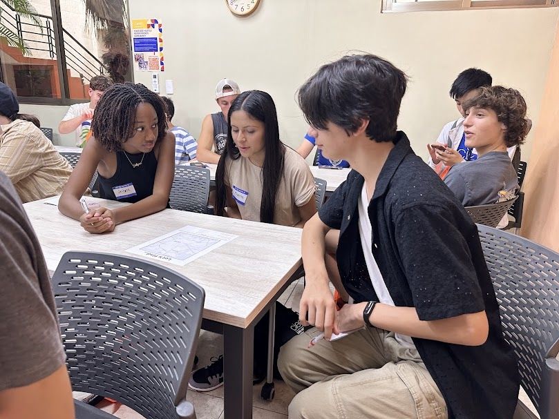 Three students sit around a table viewing a map of Merida, Yucatan. 