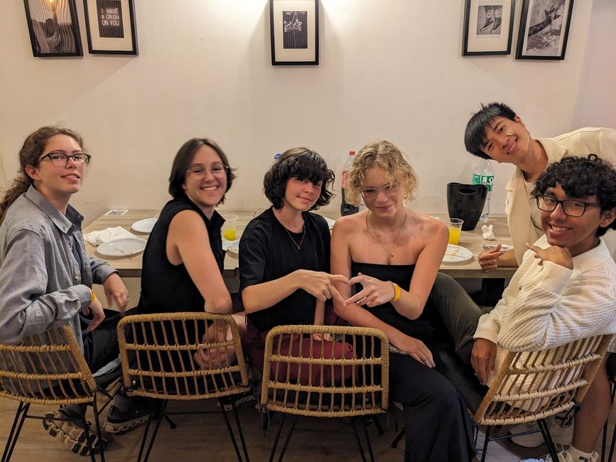 Six students sit at a table and pose for a picture, two make a heart with their hands