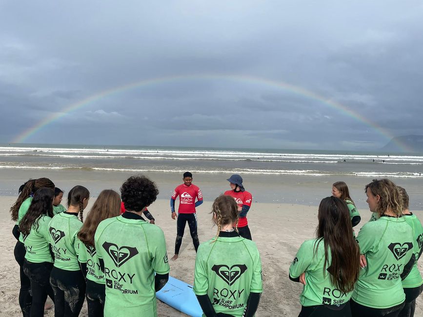 High school students learning how to surf on the beach with a rainbow above them