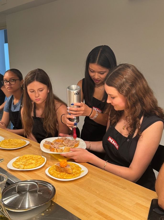 Girls using whipped cream siphon for red pepper foam.