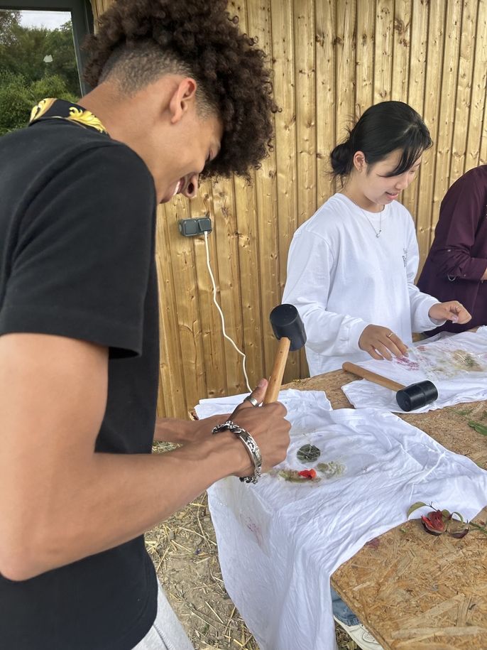 One student smiles as he works on his t-shirt design and prepares to press the flowers using the rubber mallet