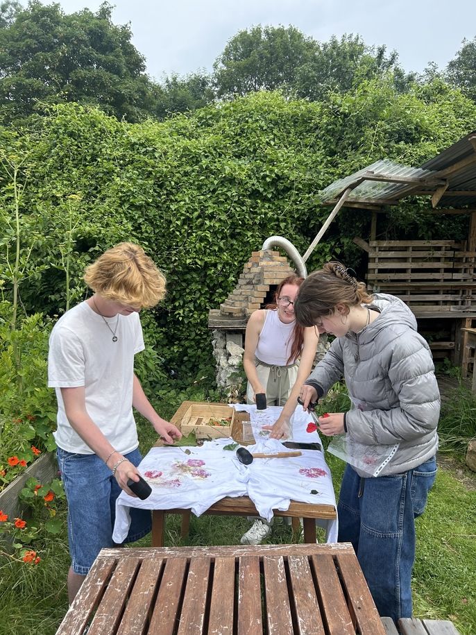 A group of three students press the flowers into their shirts using the rubber mallets