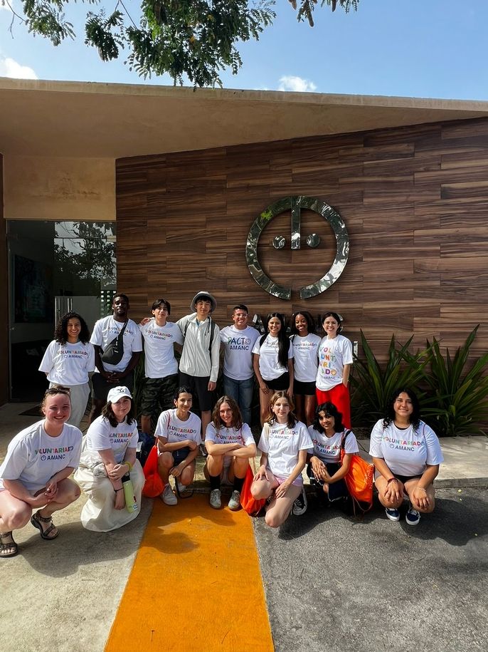 A group of students and group leaders in white t-shirts stand in front of the AMANC building in Merida, Yucatan. 