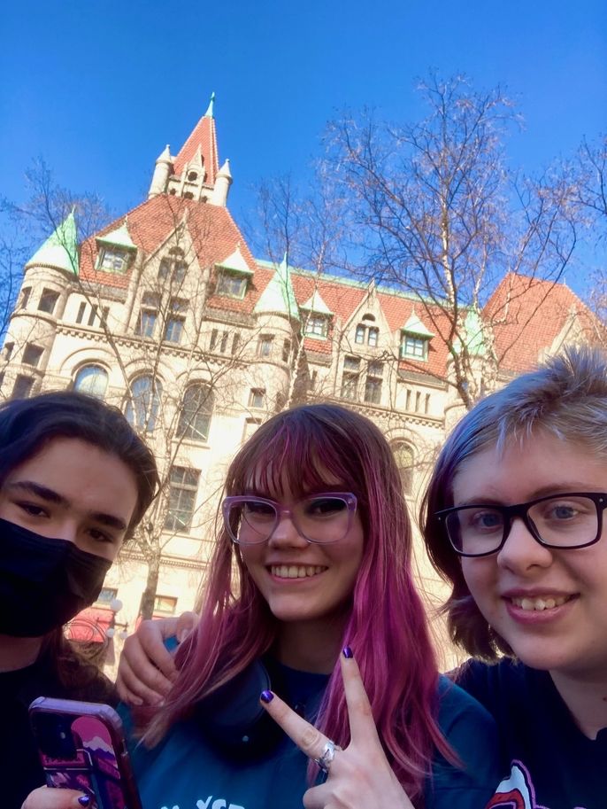 Three smiling teenagers in front of a castle with an orange top. 