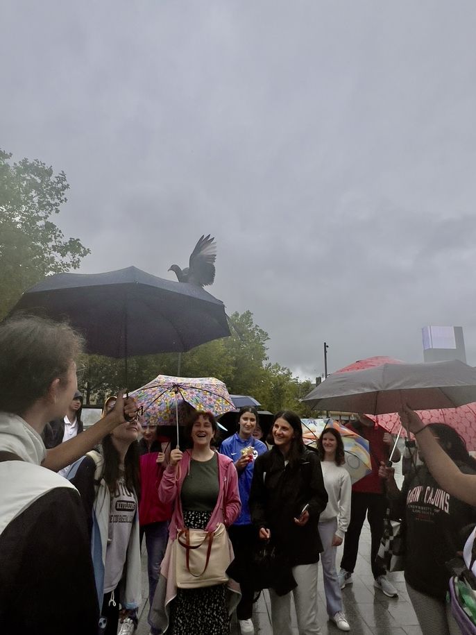 students listening to Program leader in the rain and holding umbrellas