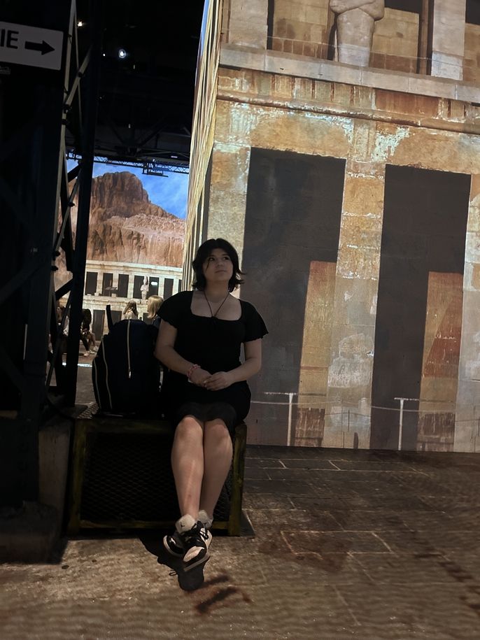 HSSA Language and Culture Student Charlotte Reyes sits and observes the light show. The projection of an Egyptian building is on the wall behind her. 