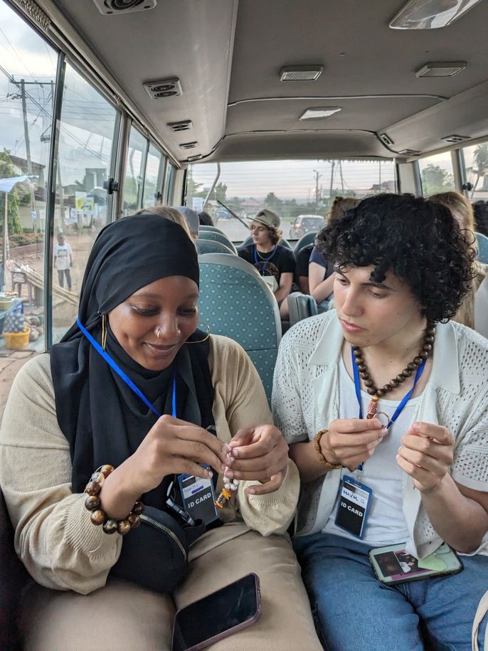 Max looks on as Monajah finishes her beading on the bus.