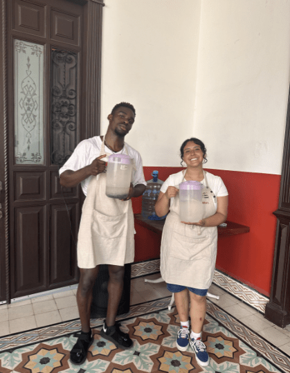 Two students wearing aprons stand side by side holding jars of water