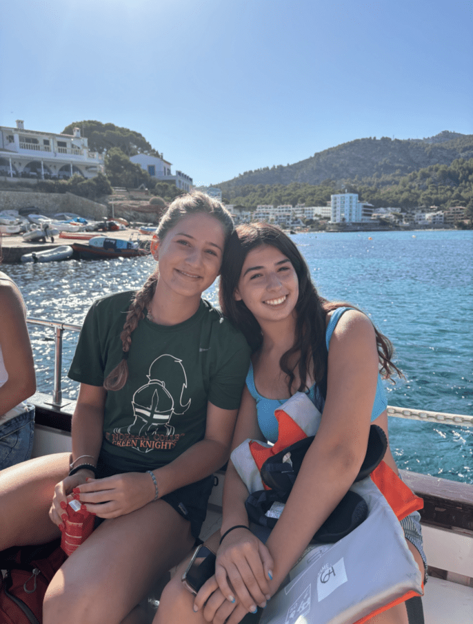 Two students pose for a picture sitting on a boat bench with the Mediterranean sea in the background