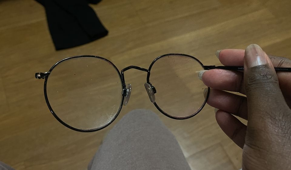 In a room against a wooden background - a hand holds a pair of glasses, with a broken hinge and no arm