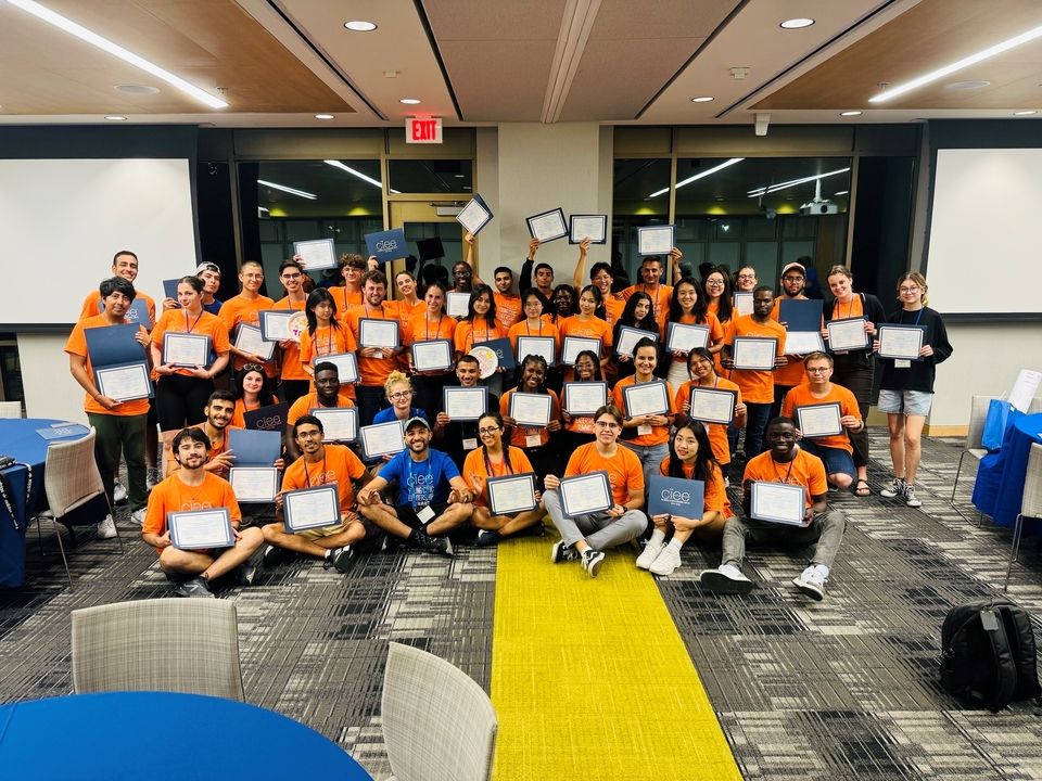 Group photo of Young Civic Leadership Summit participants indoors, proudly holding their certificates of achievement. The participants, dressed in orange CIEE t-shirts, are gathered together in a celebratory pose, showcasing their accomplishments.